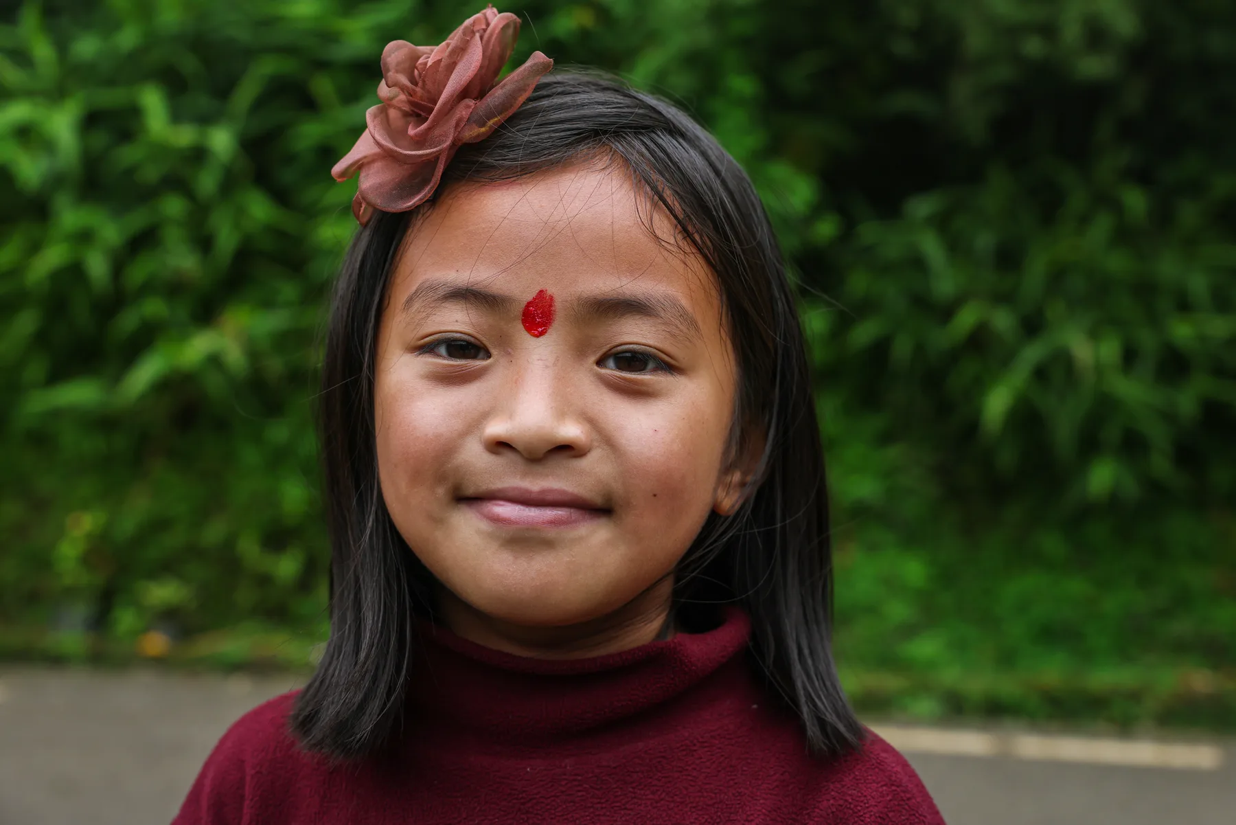 A young local resident wearing a flower and a red tika