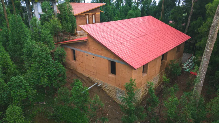 The red-roofed rammed-earth house framed by forest