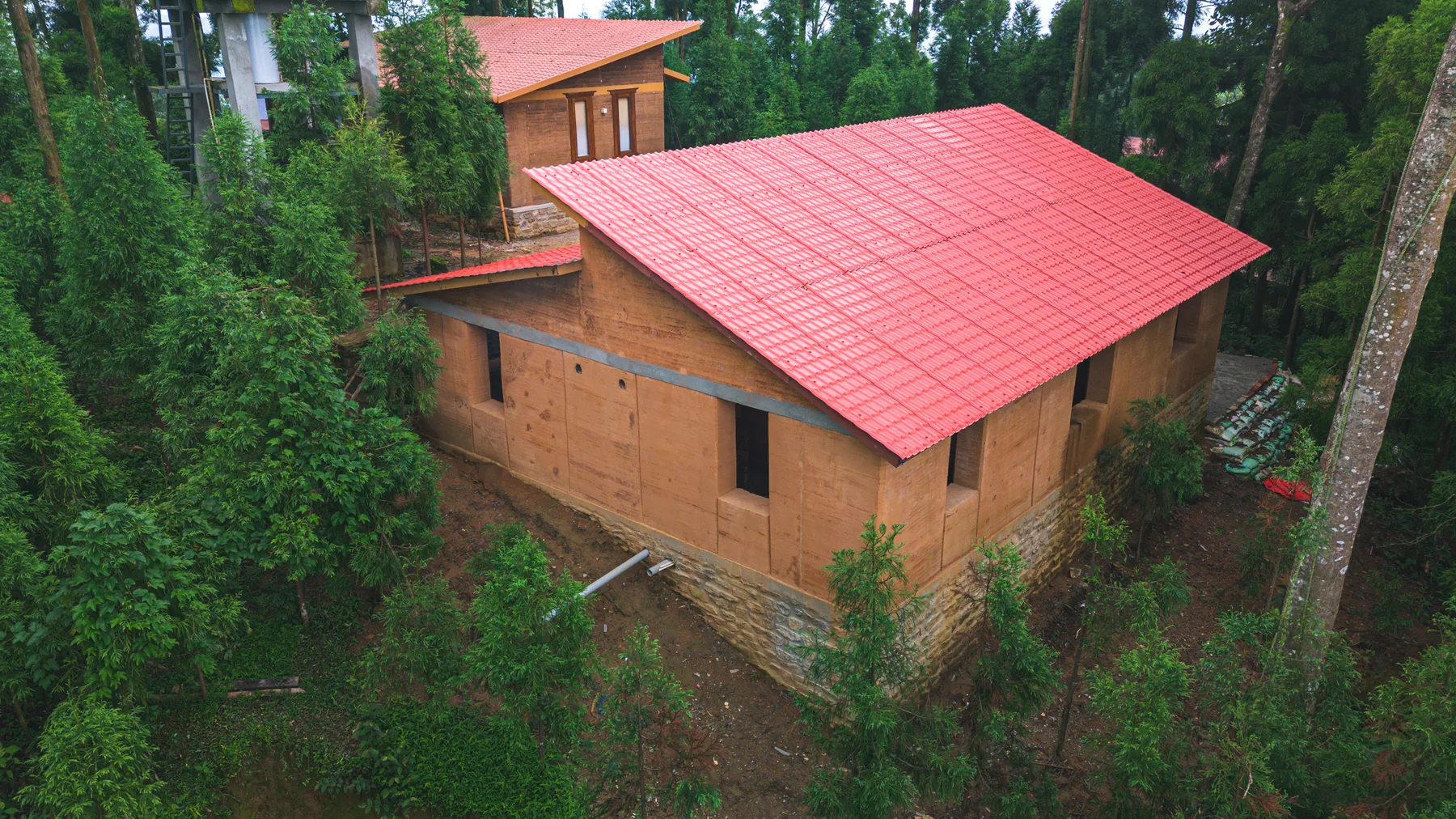 The red-roofed rammed-earth house framed by forest