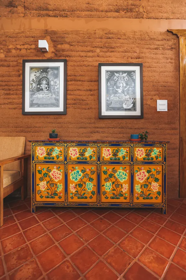 A hand-painted cabinet and framed artwork against rammed-earth walls