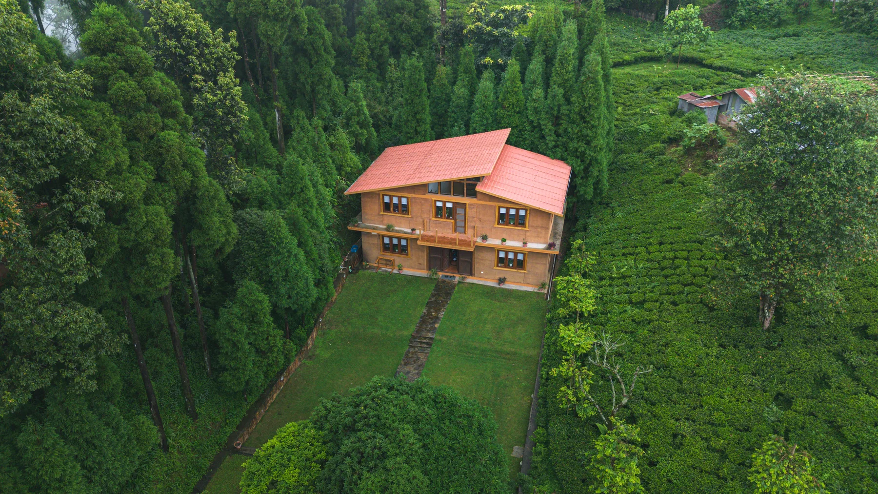The two-storey rammed-earth villa beside tall trees and tea gardens